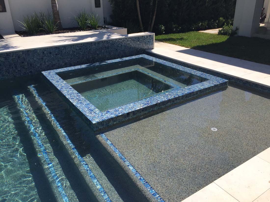 A square hot tub in the middle of a swimming pool.