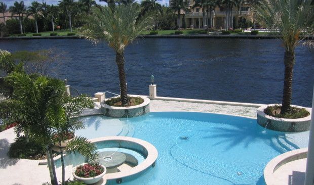 A large swimming pool surrounded by palm trees next to a body of water.