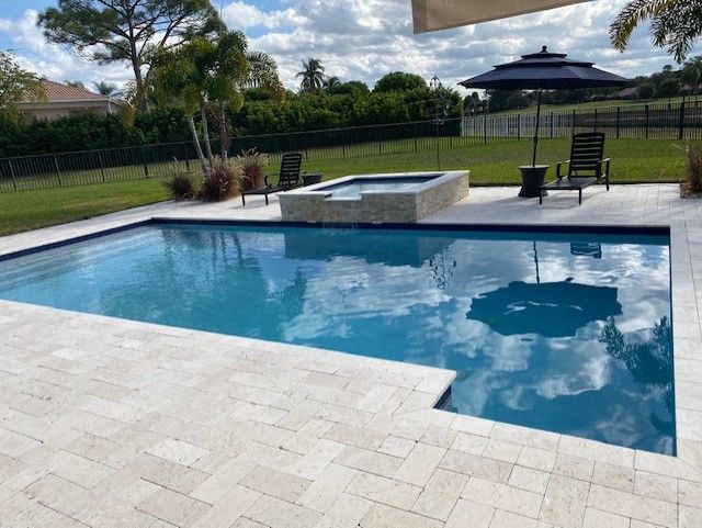 A large swimming pool surrounded by chairs and umbrellas in a backyard.