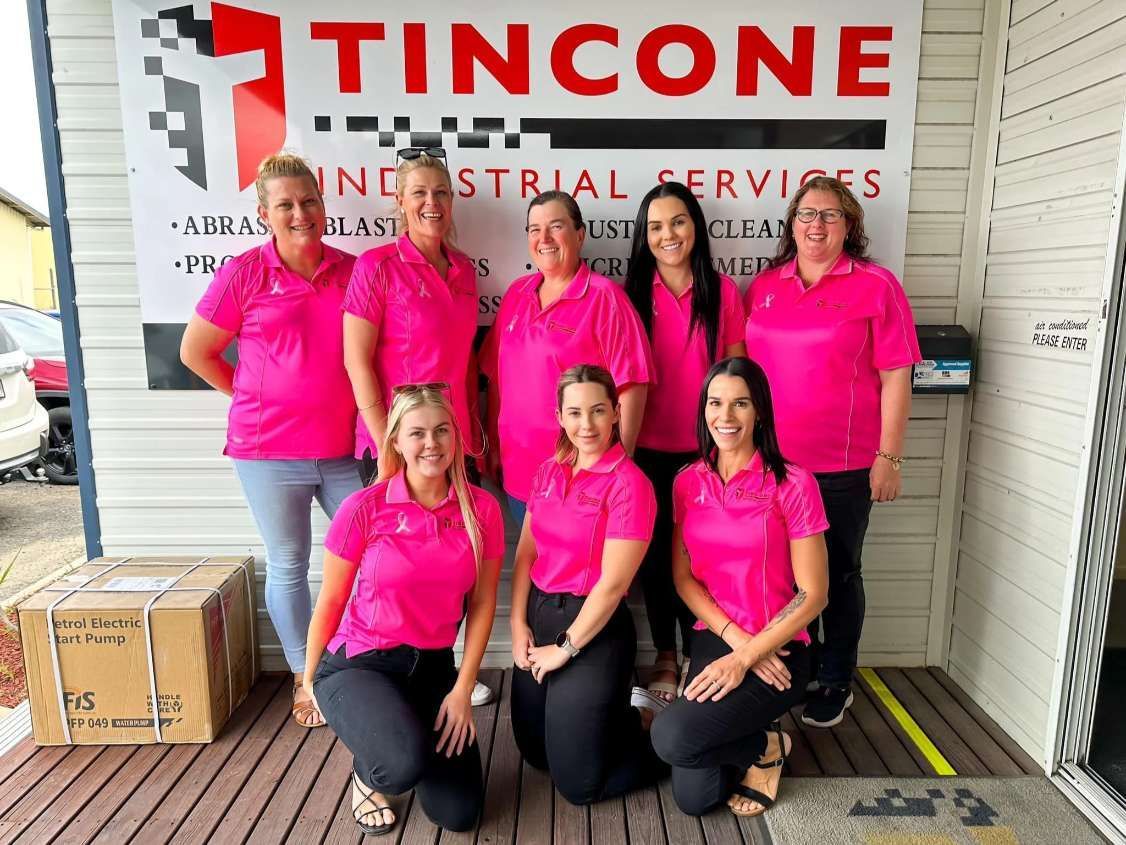 Group of Women in Pink Shirts Posing in Front of a Business Sign — Tincone Pty Ltd in Paget, QLD