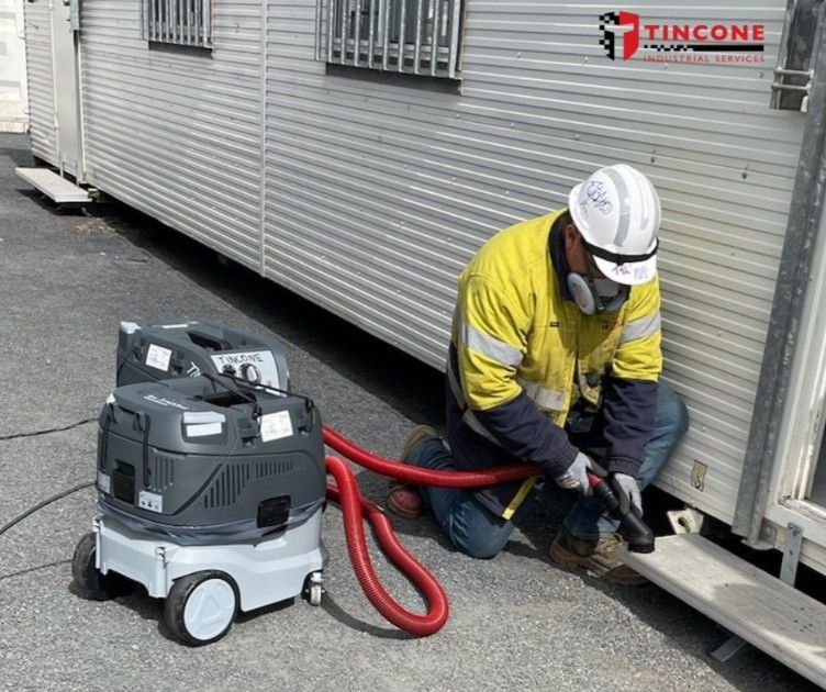 A Construction Worker in Protective Gear Uses a Vacuum Near a Trailer — Tincone Pty Ltd in Paget, QLD