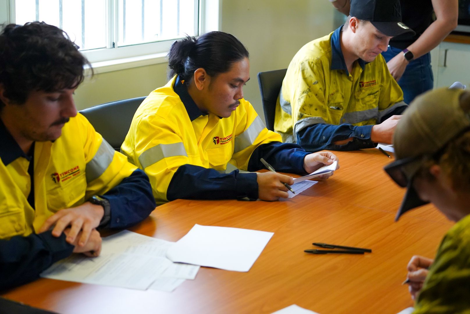 Four Construction Workers in Yellow Safety Vests Sit Around a Table, Focused on Paperwork — Tincone Pty Ltd in Paget, QLD