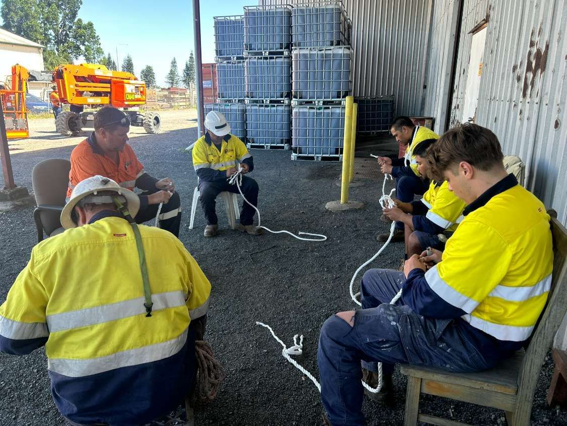 Group of Workers in Yellow Safety Vests Learning to Tie Knots Outdoors on Gravel — Tincone Pty Ltd in Paget, QLD