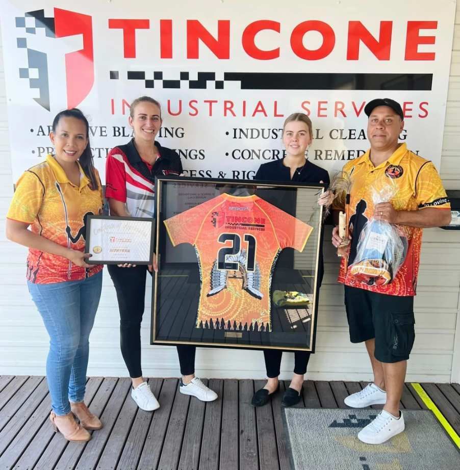 Four People Pose With a Framed Jersey and Gifts — Tincone Pty Ltd in Paget, QLD
