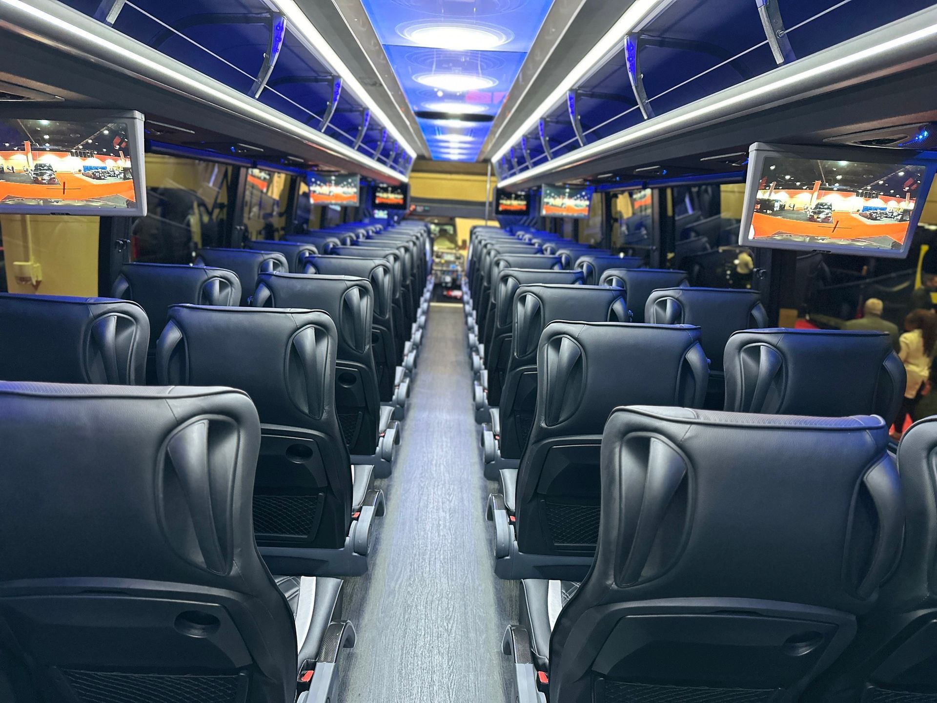 A bus with a lot of seats and televisions on the ceiling