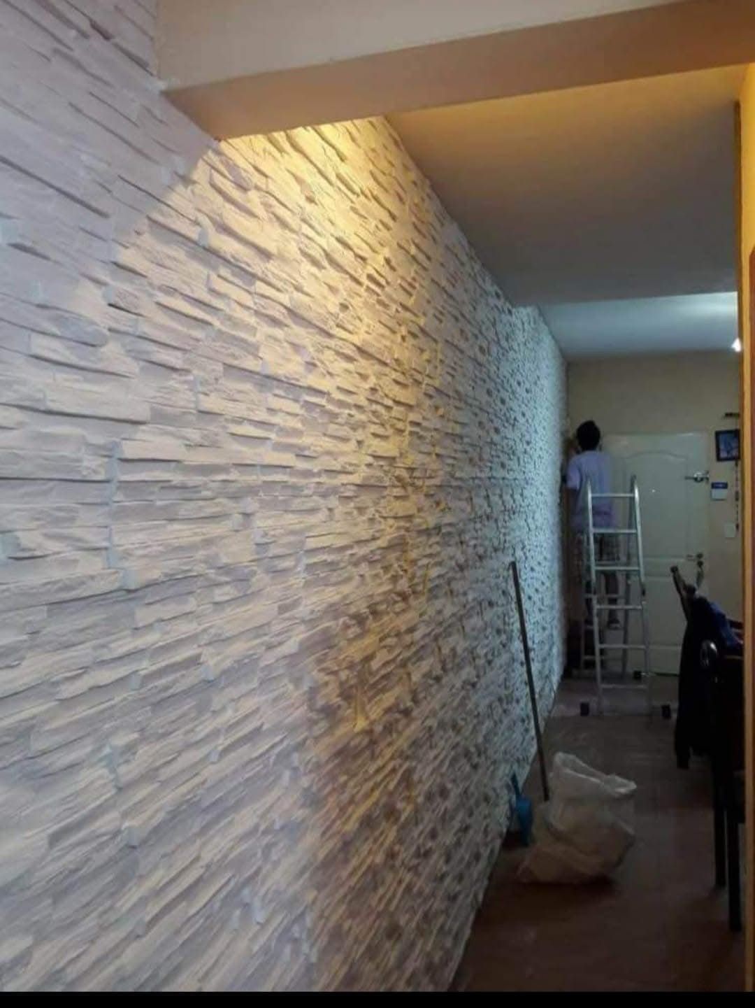 Pared blanca texturizada con una persona trabajando en ella en una escalera. Pasillo interior.