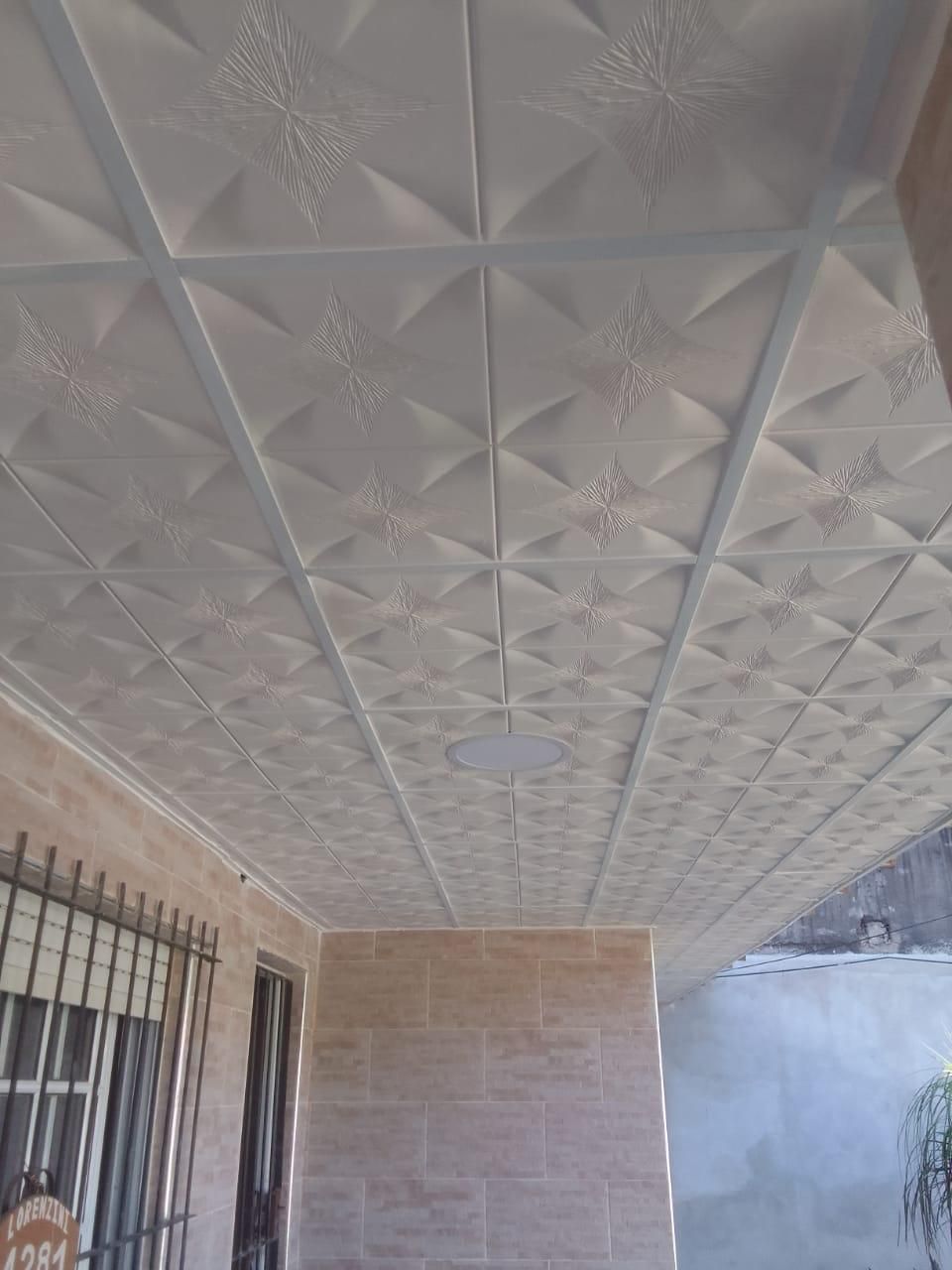 Techo de porche cubierto con azulejos texturizados blancos y vigas de soporte grises.