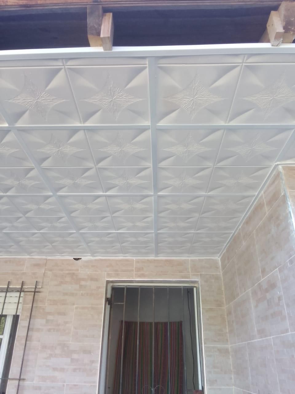 Techo exterior con azulejos blancos estampados, encima de una puerta y paredes de azulejos beige.