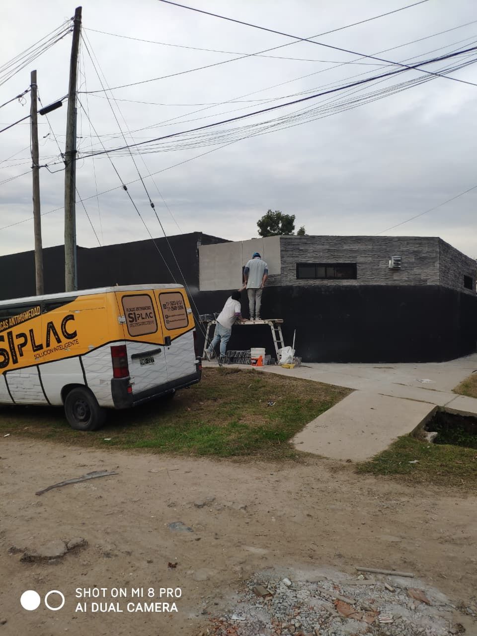 Dos trabajadores pintando una valla negra junto a un edificio.