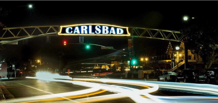 Nighttime view of Carlsbad archway, with illuminated sign over a street with blurred car lights.