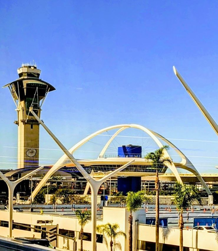 LAX airport terminal with control tower and iconic arches, blue sky, palm trees.