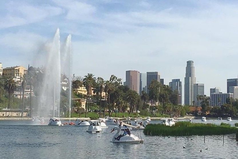 Lake with fountain and swan boats; Los Angeles skyline in the background.