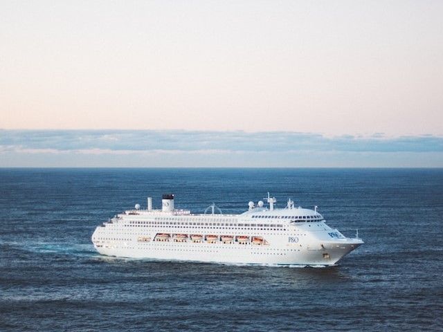 Cruise ship sailing on blue water, under a pale blue sky.