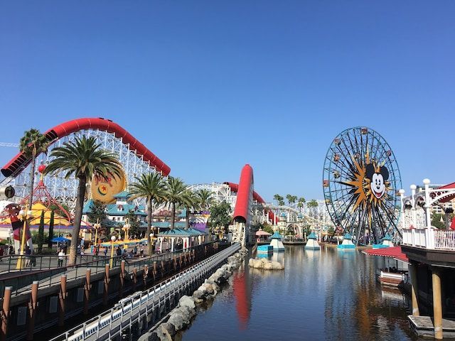 Roller coaster and Ferris wheel at Pixar Pier, Disneyland, with water and blue sky.