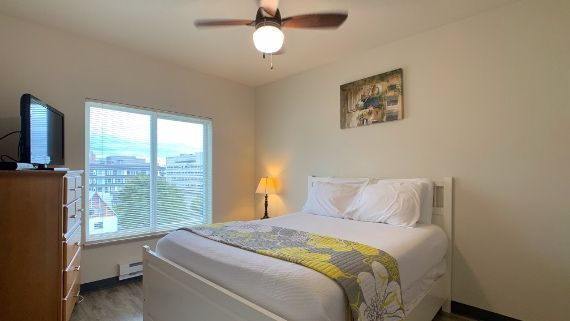 A bedroom with a bed , dresser , television and ceiling fan.