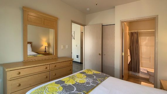 A bedroom with a bed , dresser , mirror and bathroom.