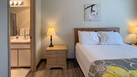 A bedroom with a bed , nightstand , lamp and bathroom.