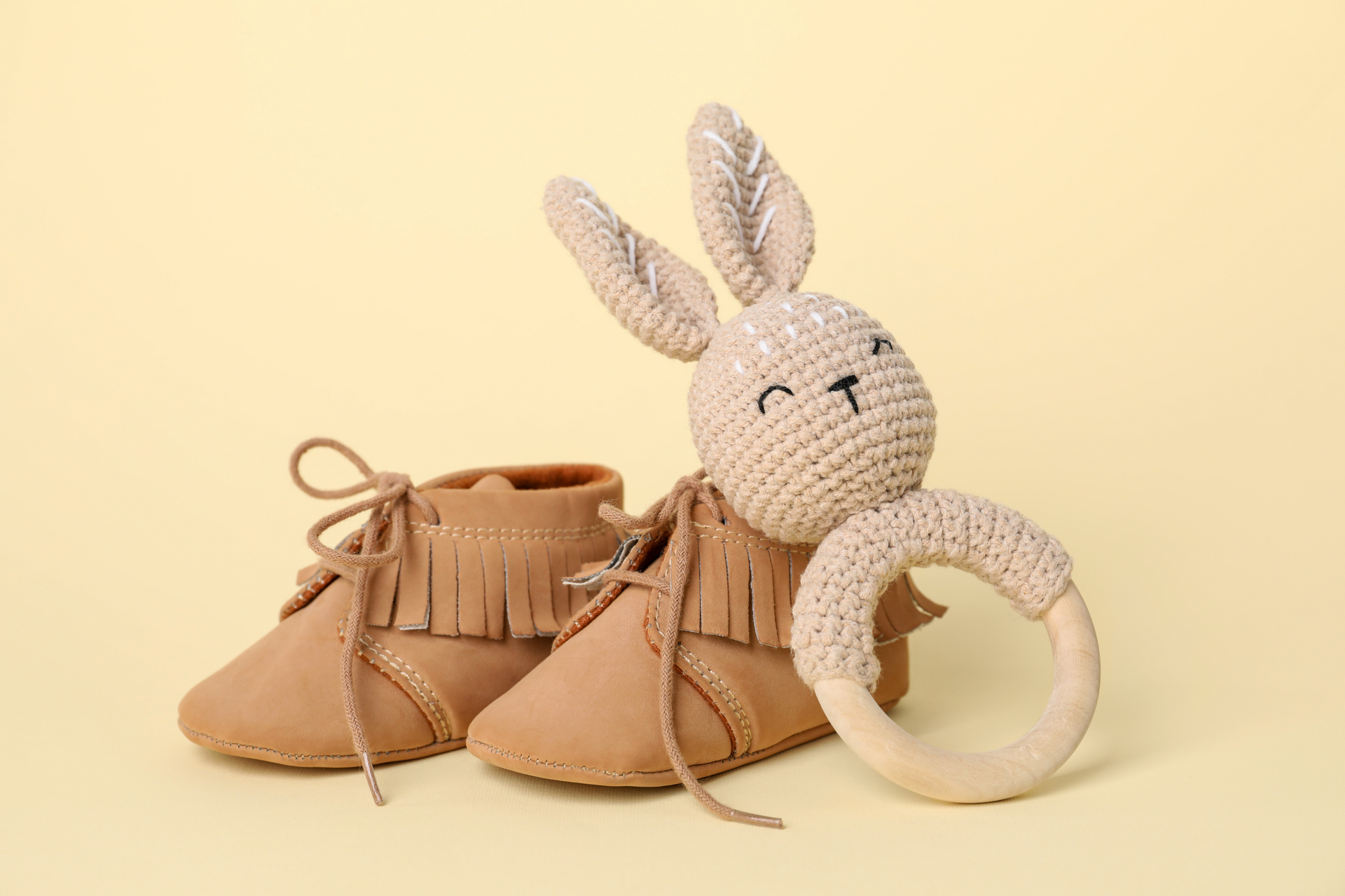 Une paire de chaussures pour bébé et un hochet lapin au crochet sur fond jaune.