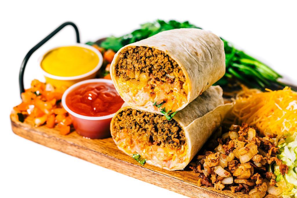 two burritos are stacked on top of each other on a wooden cutting board .