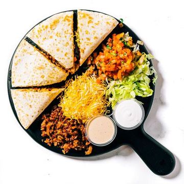a black plate topped with quesadillas , meat , lettuce , sour cream and salsa