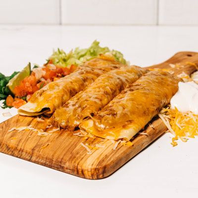 a wooden cutting board topped with three enchiladas covered in cheese and sour cream