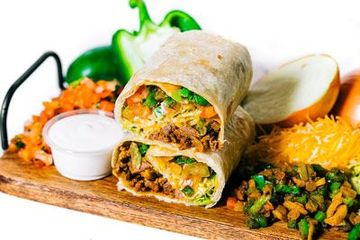 fajita burrito sitting on top of a wooden cutting board next to vegetables