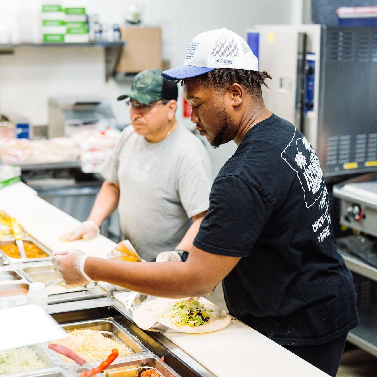 a man wearing a columbia hat prepares food in a kitchen