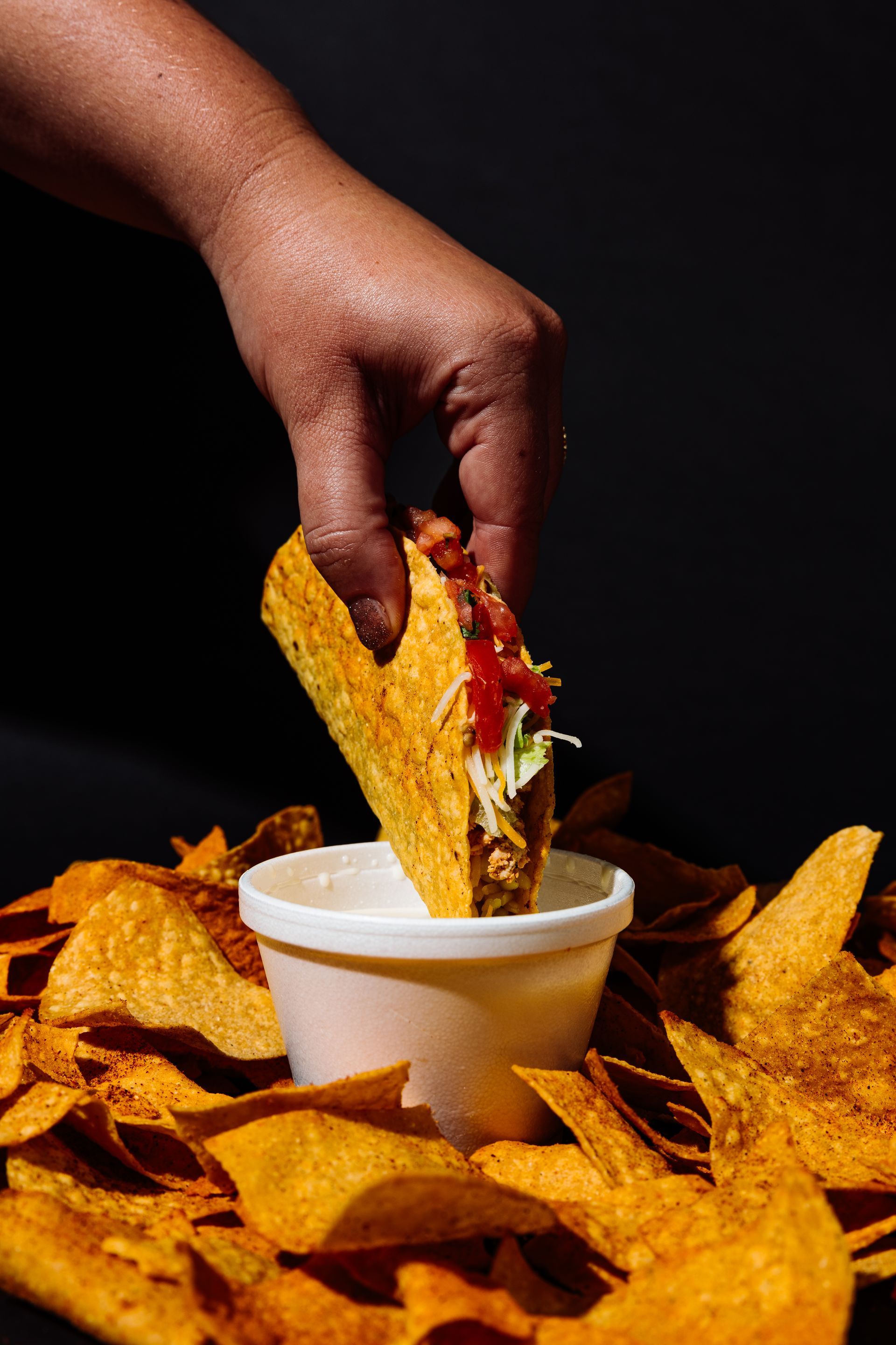 A person is dipping a taco into a bowl of nachos.