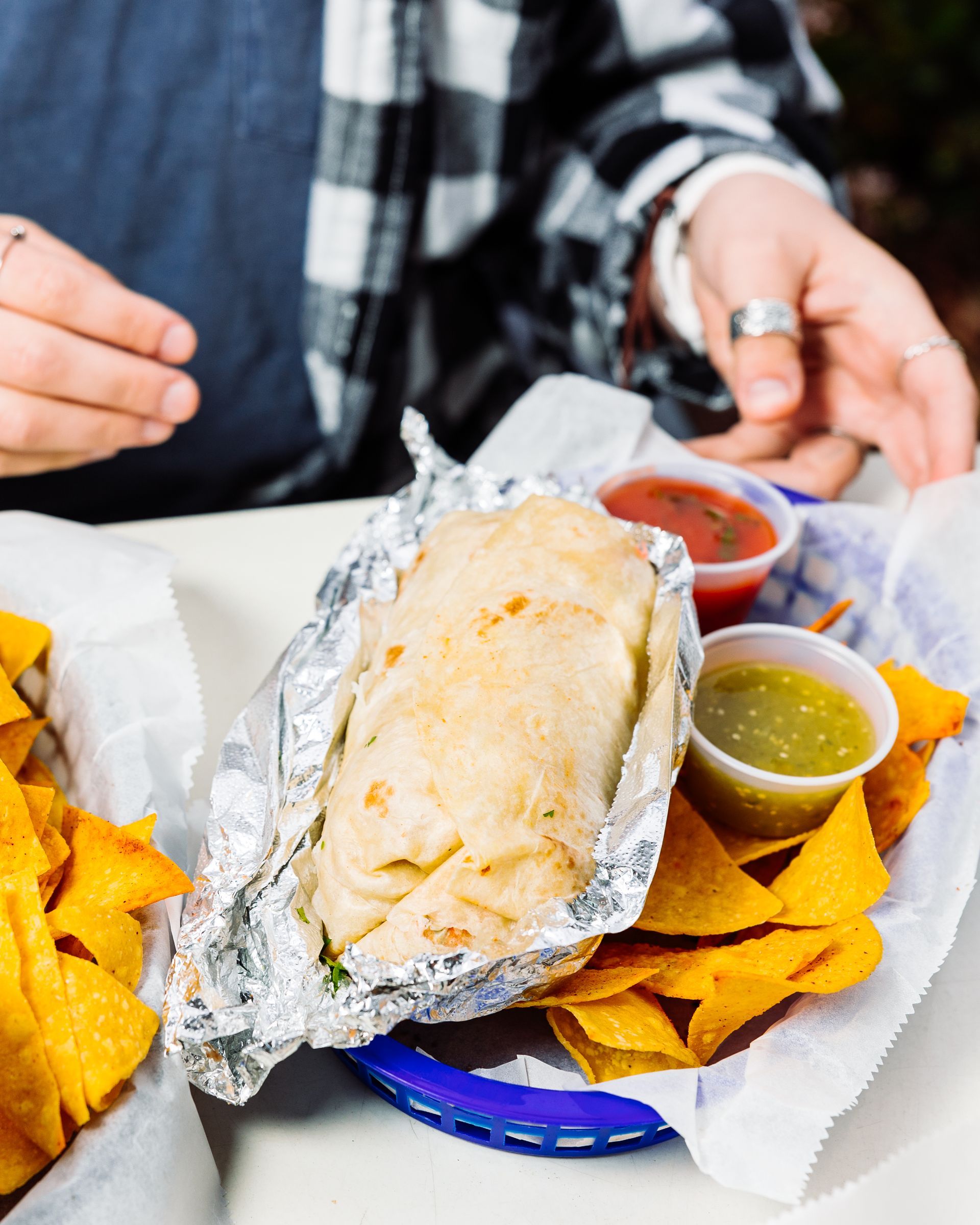A person is sitting at a table eating a burrito and nachos.
