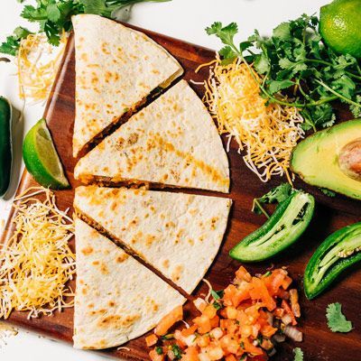 a wooden cutting board topped with quesadillas and vegetables