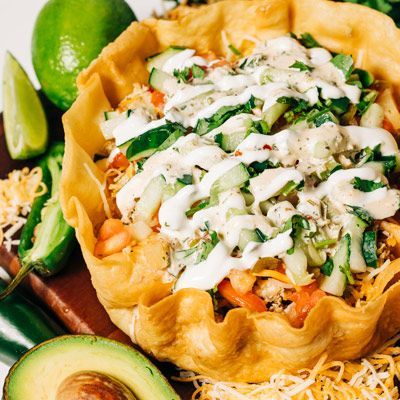 a close up of a taco salad with avocado and limes on a table