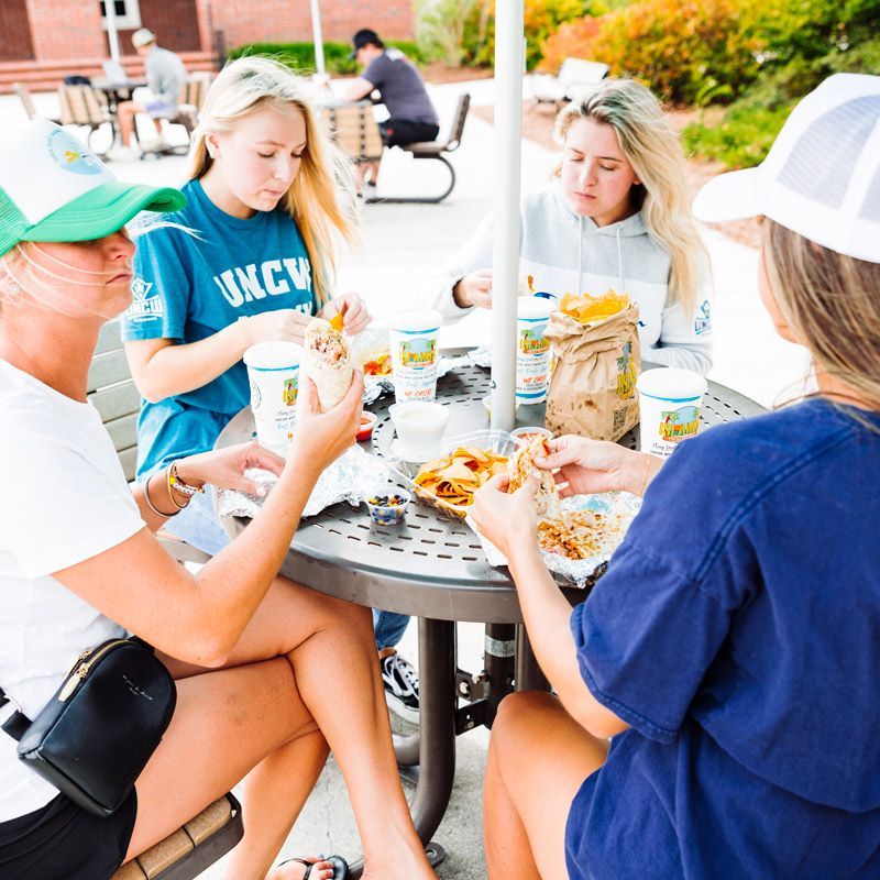 a girl wearing a college shirt sits at a table eating mexican food