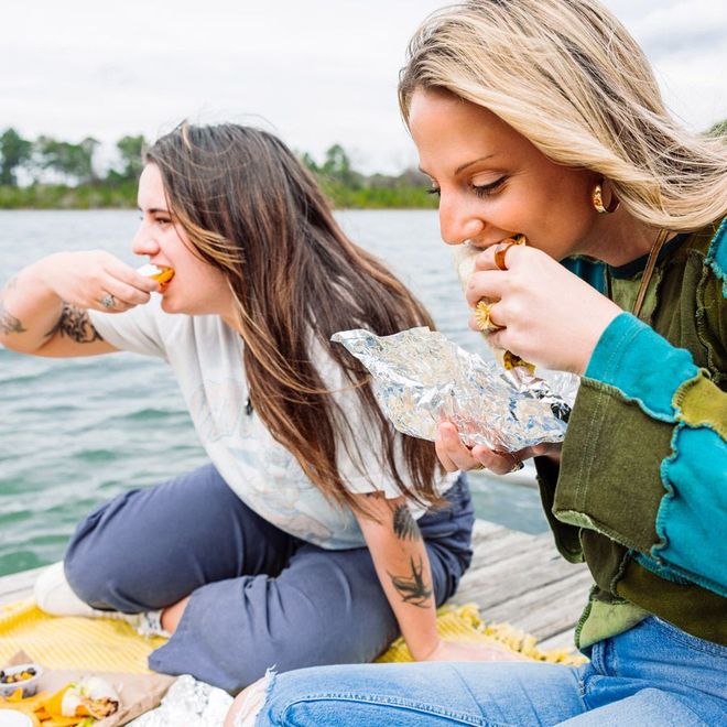 two women are sitting on a dock eating food