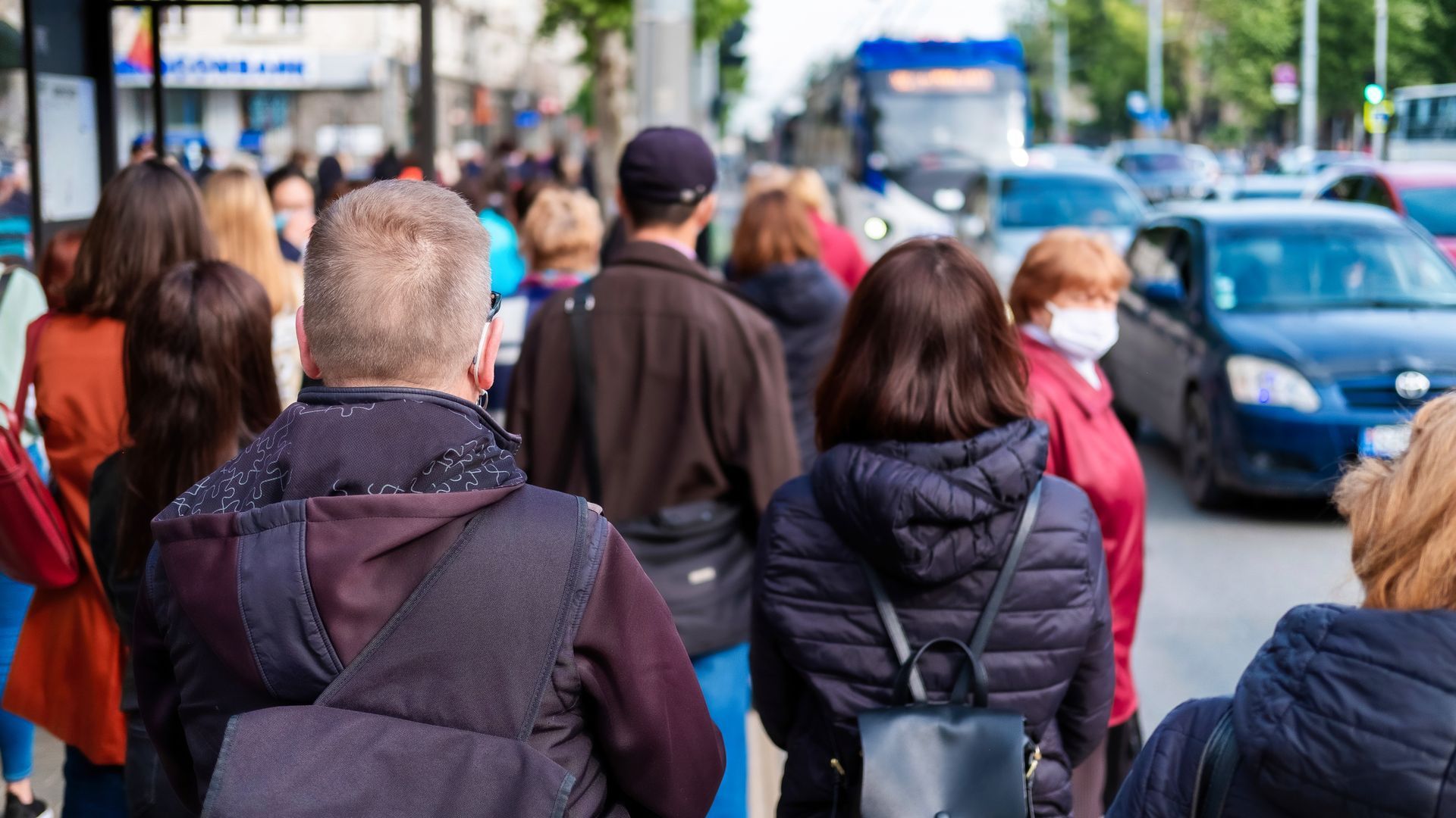 Folk går på et fortov i nærheden af ​​trafik, hvor én person bærer en rød ansigtsmaske.