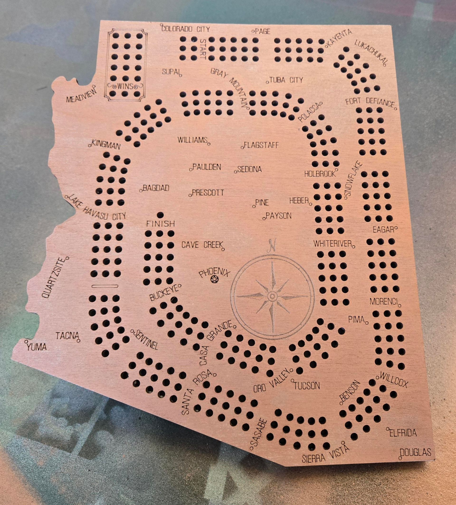 Wooden cribbage board shaped like the state of Arizona with numerous holes for pegs, and a compass rose.
