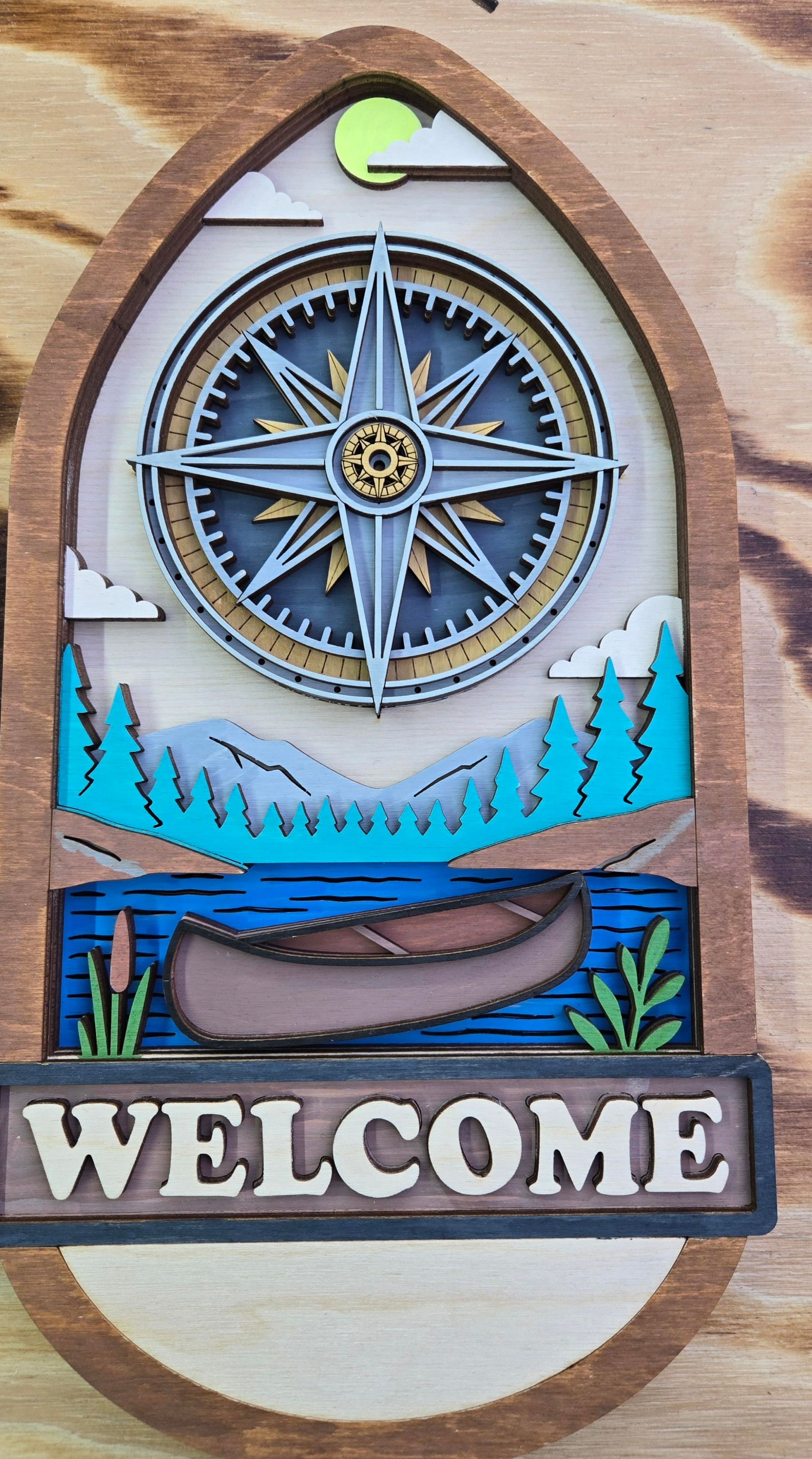Wooden layered sign with compass, mountains, lake, canoe, and 