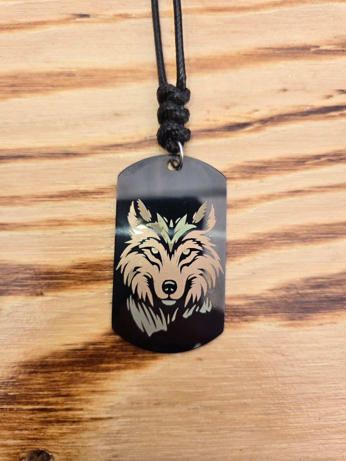 Black dog tag necklace with wolf face etched in silver on a wood background.