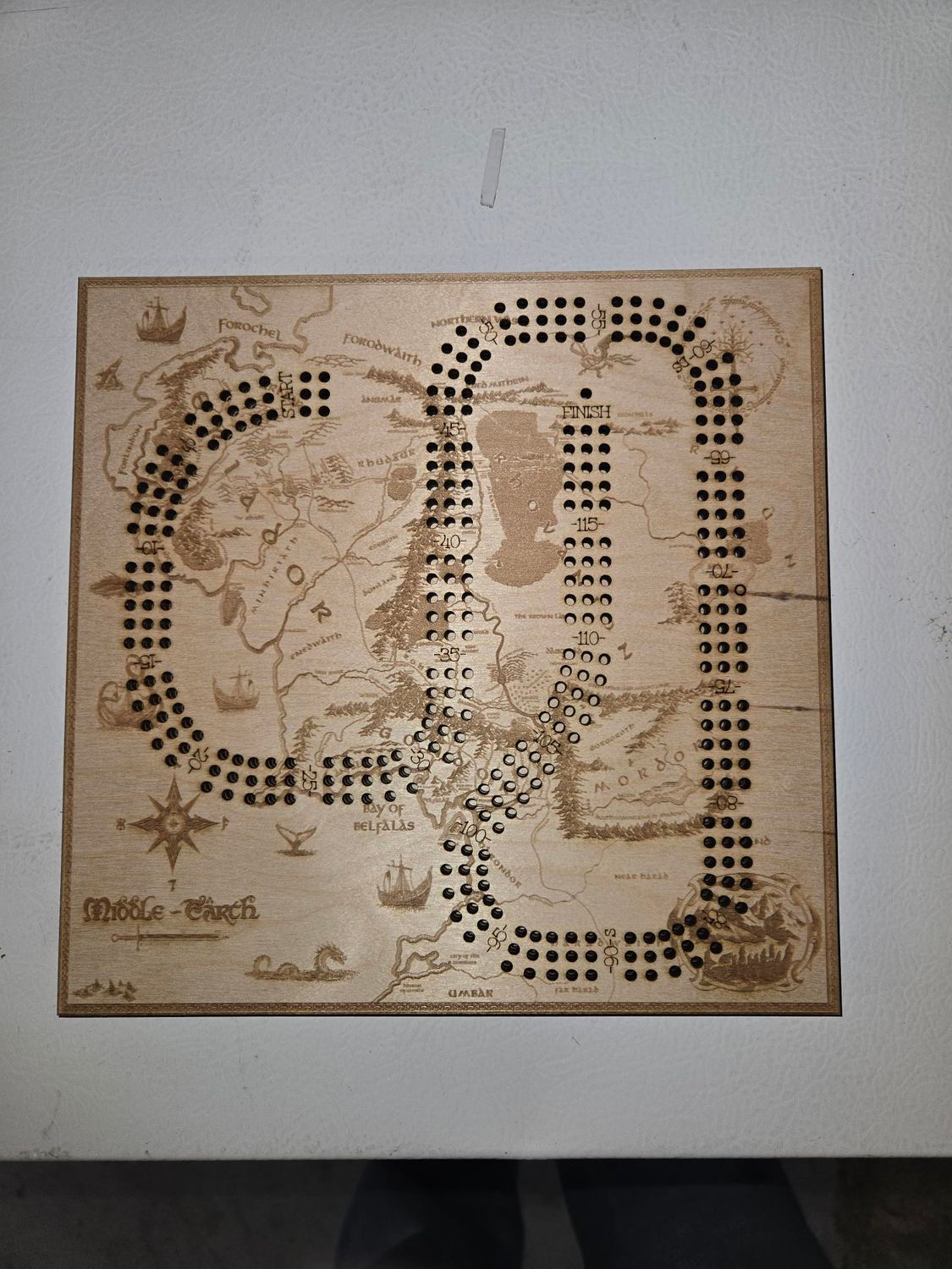 Wooden game board, laser-etched map with paths, holes for pegs, and text 