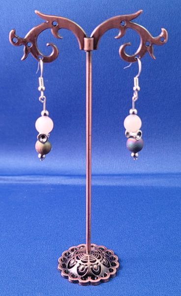 Pair of drop earrings with white and green beads, displayed on a copper-colored stand on a blue background.
