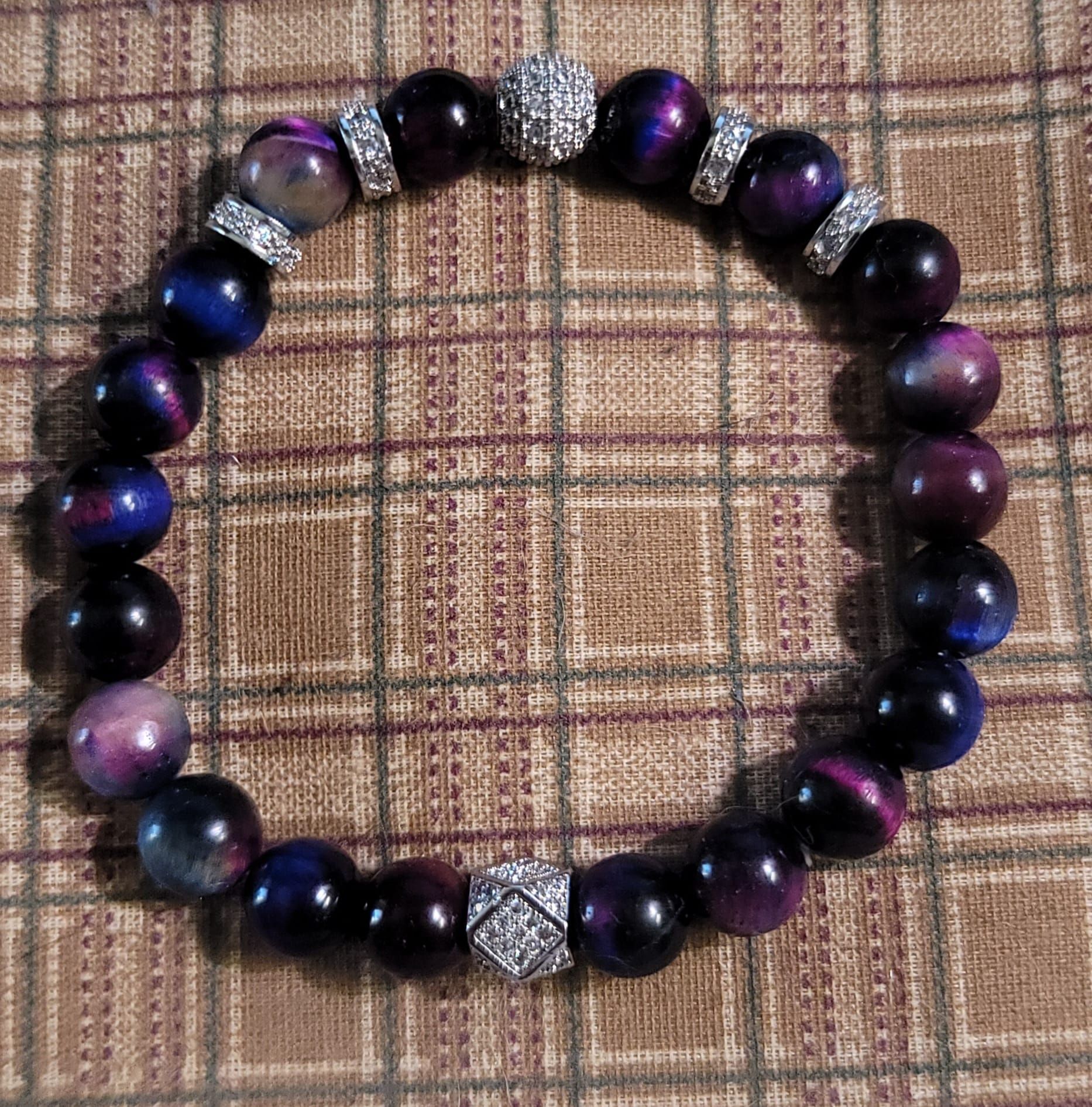 Purple and blue beaded bracelet with sparkly silver accents on plaid fabric.
