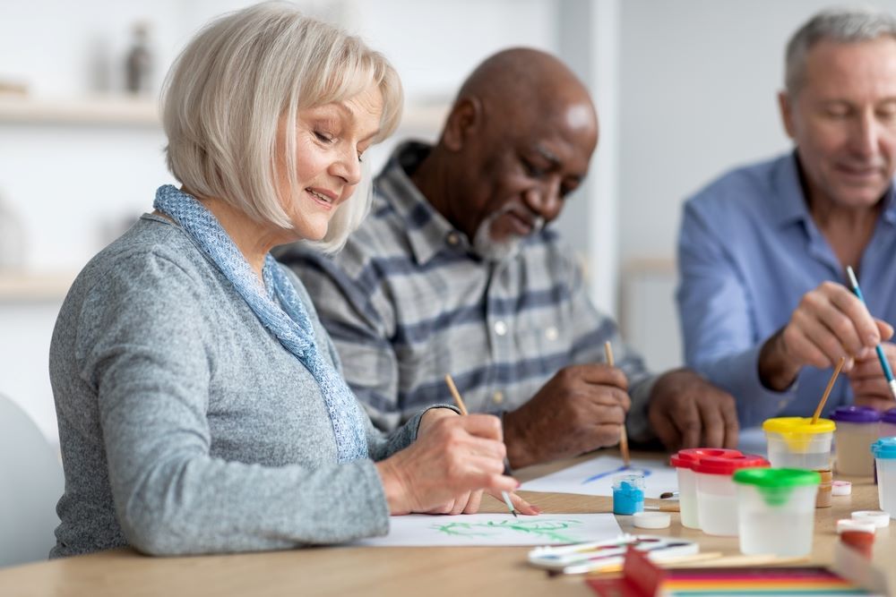 A Group of Elderly People Are Sitting at a Table Painting — Eleos Support Services In Lavington, NSW