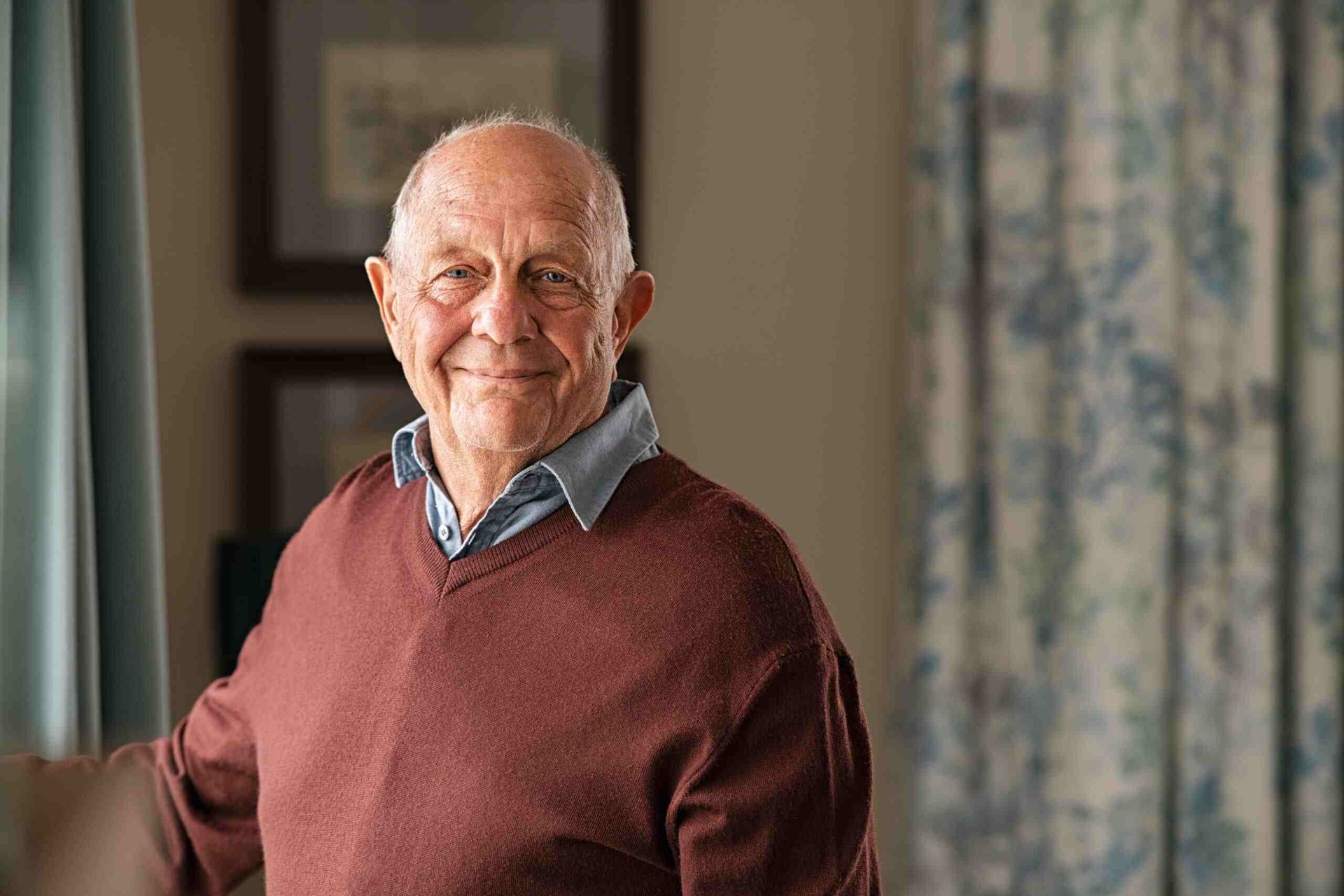 An elderly man in a red sweater is standing in front of a window — Eleos Support Services In Lavington, NSW