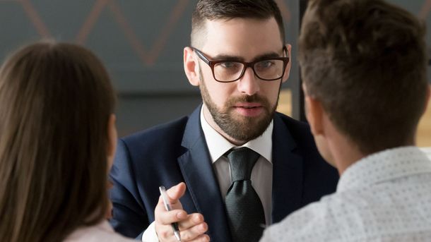 Man in suit with glasses advises a couple in an office setting.