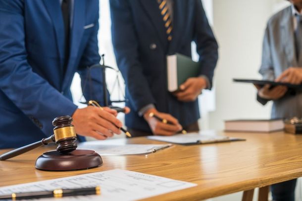Lawyers in suits at a table, reviewing documents, gavel in foreground.