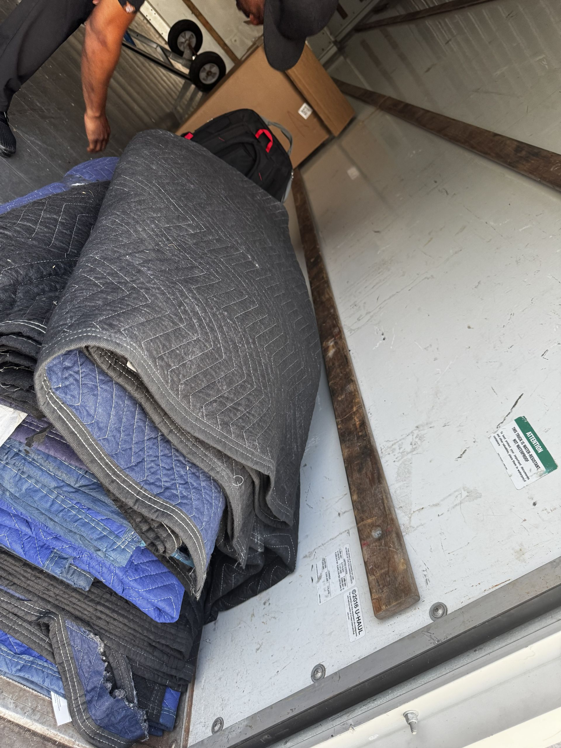 A stack of folded blue and black moving blankets inside a truck, with a person standing nearby.
