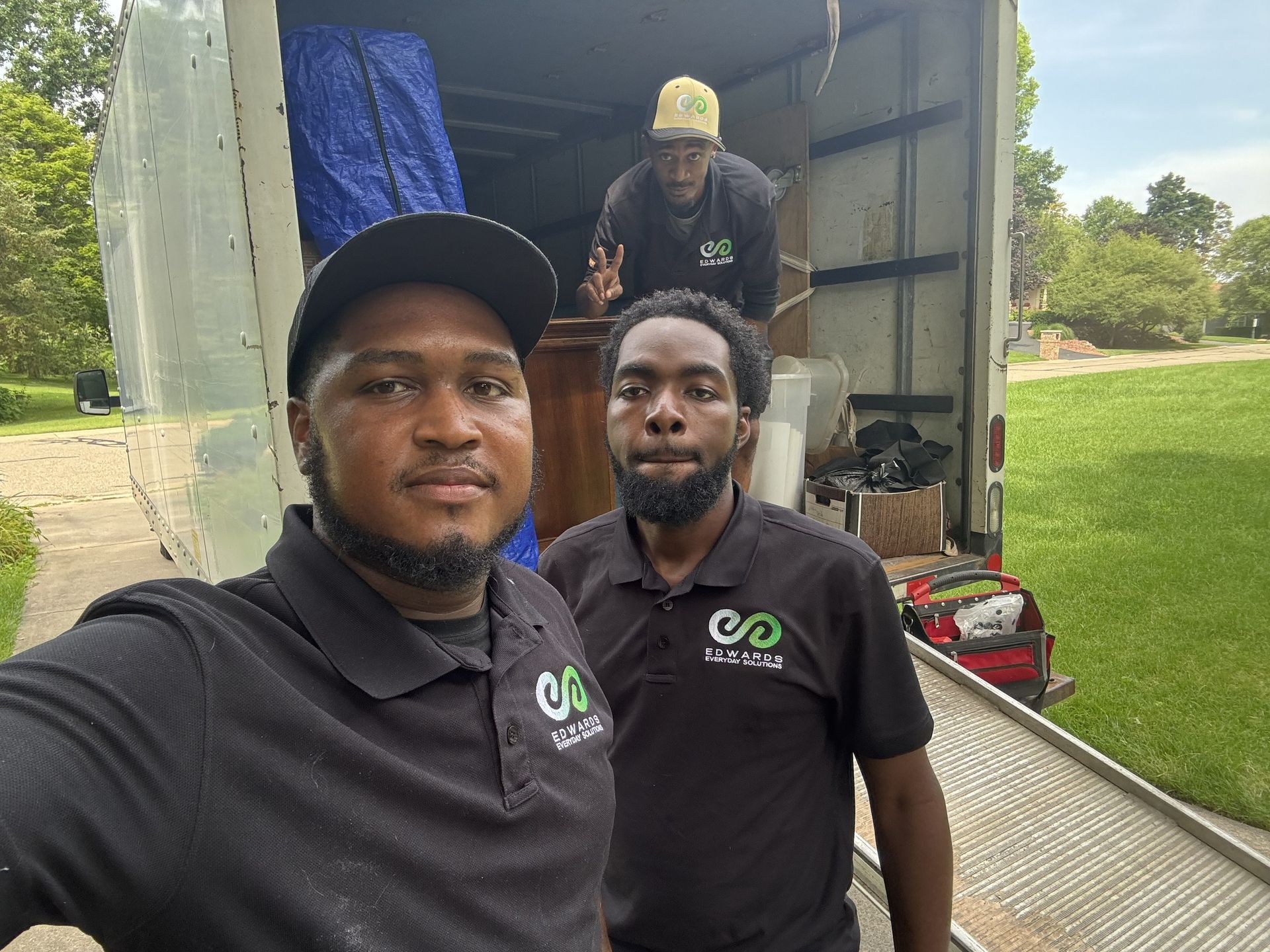 Three movers in matching black company shirts stand in and near an open moving truck outdoors.
