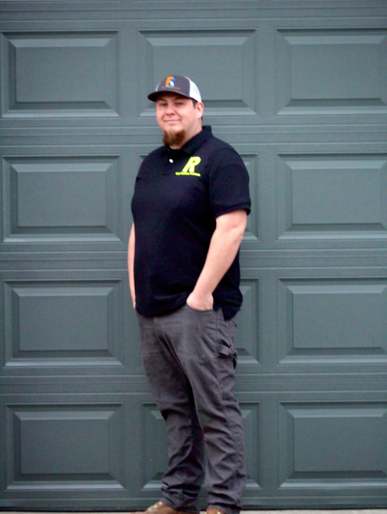 A man wearing a hat and a black shirt is standing in front of a garage door.