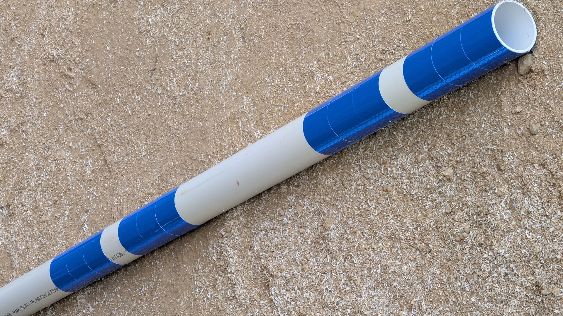 A white PVC pipe resting on a textured concrete surface, featuring repeating blue and gray striped tape patterns.