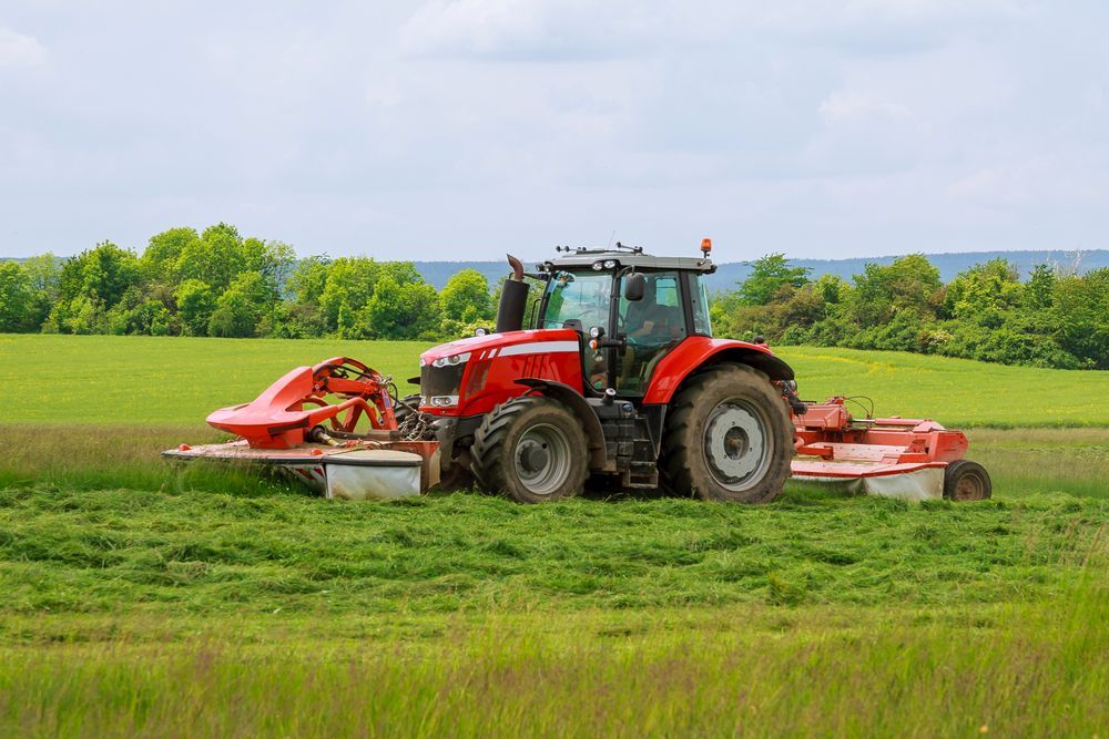 Red Tractor Mowing a Green Field, With Trees in the Background — Jemal Enterprises In Finch Hatton, QLD