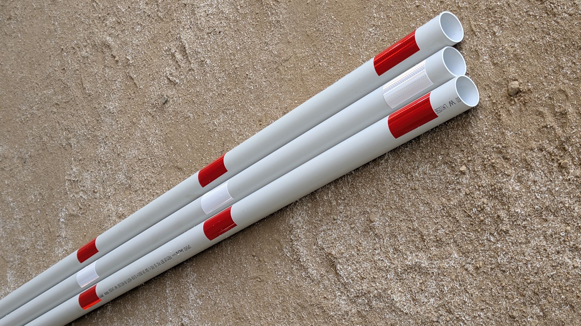 Three white pipes, each marked with repeating red rectangular bands, laid side-by-side on a textured beige surface.